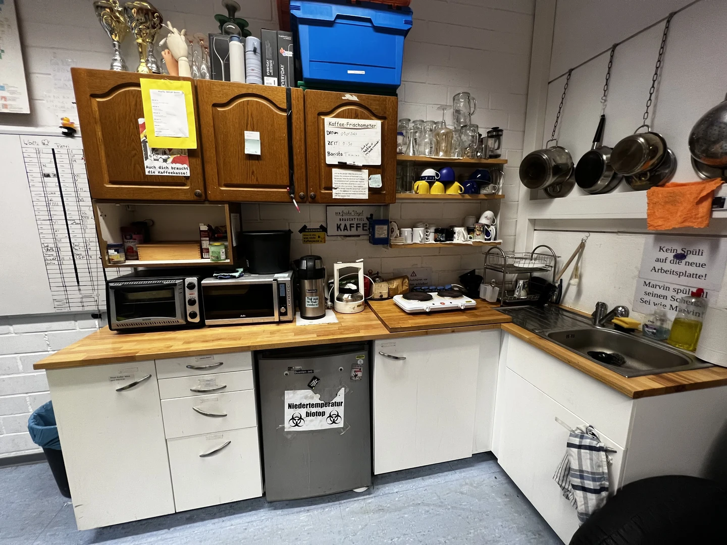 Eine Wissenschaftlerin und ein Wissenschaftler arbeiten hinter einer Glasfassade und mischen Chemikalien mit Großgeräten.